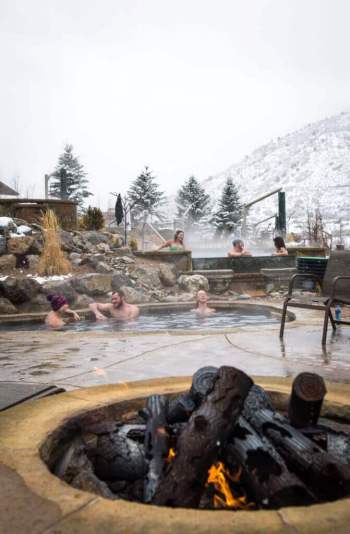 Fire-pit-with-groups-soaking-in-background-at-Iron-Mountain-Hot-Springs-vertical-671x1024
